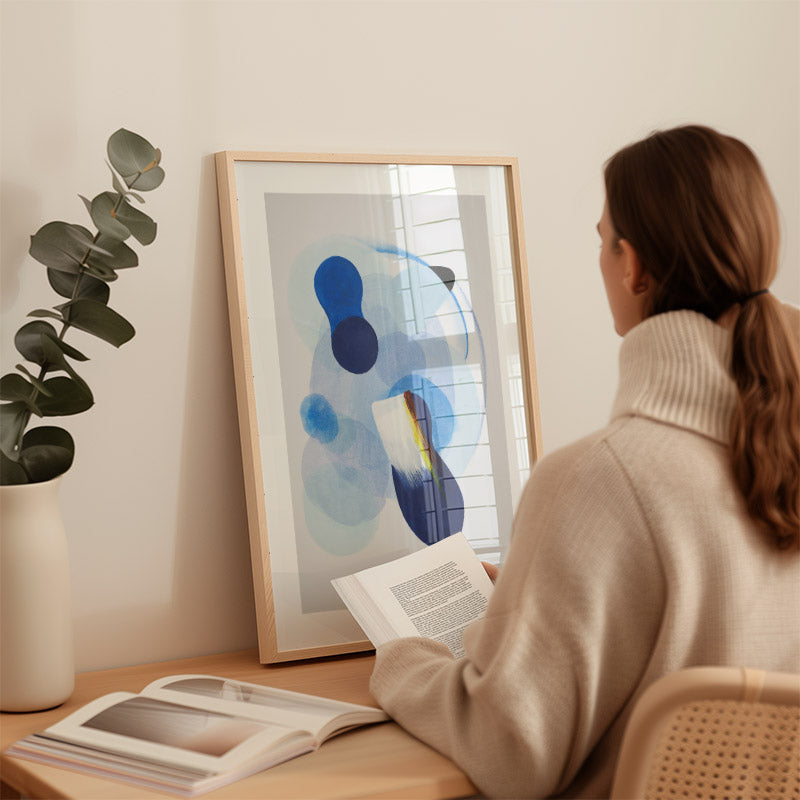 Woman sitting at a desk reading a book with abstract art and a plant in the background