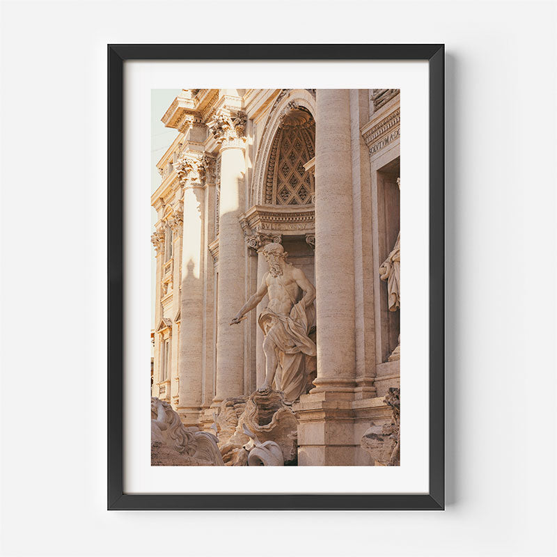 A framed art print featuring a photograph of the ornate Baroque facade of the Trevi Fountain in Rome, with a classical statue and warm beige stone architecture. The print is framed with a white mat and a modern black frame, shown against a clean white background.