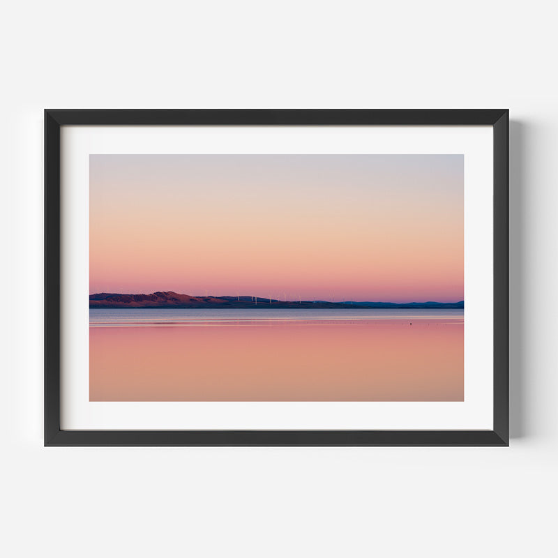 Framed artwork of a landscape with a pink and purple gradient sky over water.