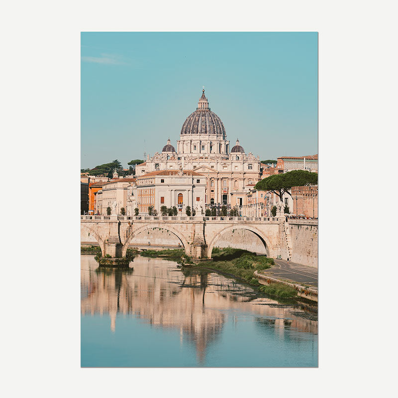 A vertical photographic print of St. Peter's Basilica in Vatican City, featuring the large dome and bridge over the Tiber River with reflections under a clear blue sky.