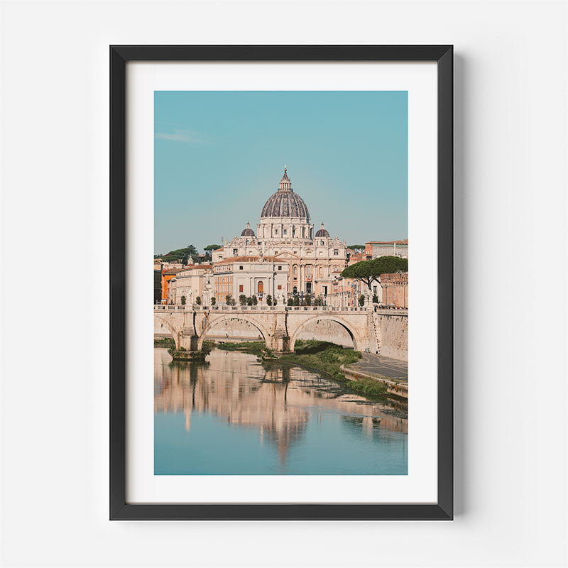 A framed art print of St. Peter's Basilica in Rome, featuring a black frame, white mat, and a photograph of the basilica and Tiber River under a clear blue sky.