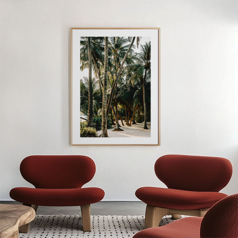 Two red chairs in a room with a framed picture of palm trees on the wall.