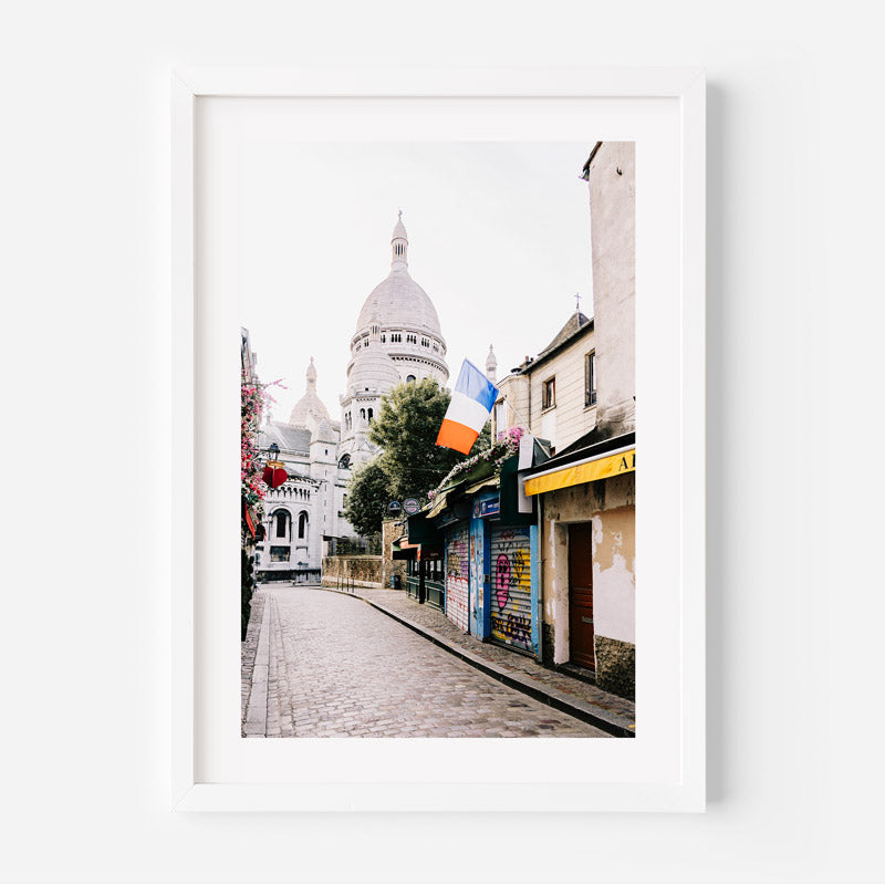 Framed photograph of a street scene with a prominent building, colorful flags, and shops.