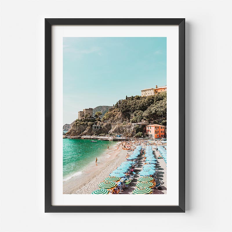 Framed photograph of a beach scene with umbrellas and buildings on a hillside.