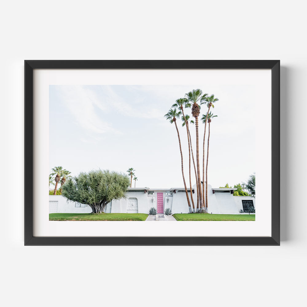 Framed photograph of a house with palm trees on a white wall