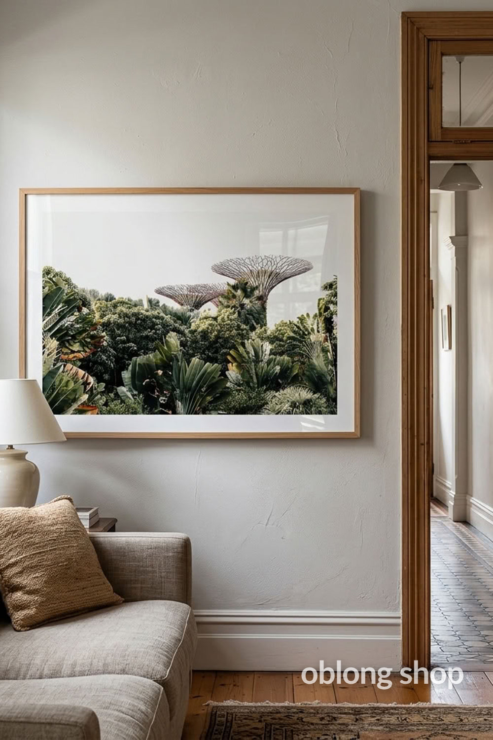 A framed botanical art print of lush green plants and mushroom-like forms, displayed on a light gray wall above a beige sofa in a modern interior setting.