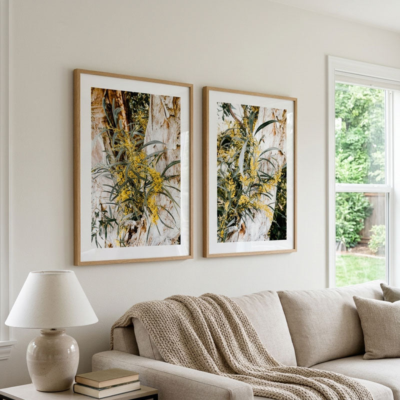 Two framed botanical art prints with yellow flowers hang on a light beige wall above a neutral sofa in a styled living room.