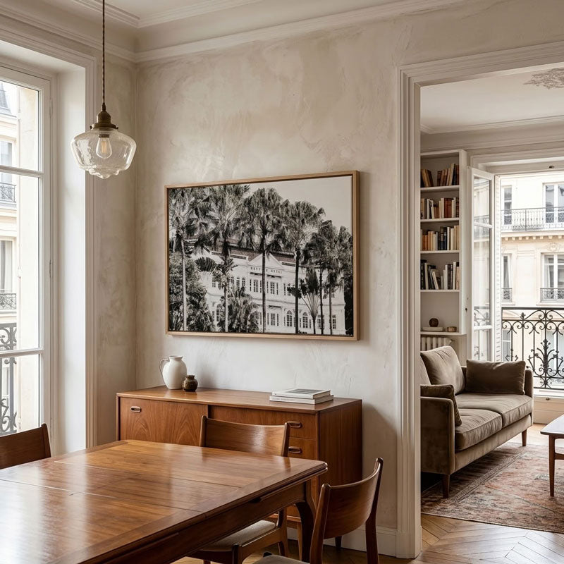 A black and white framed art print depicting a classic Parisian building and trees, displayed on a textured beige wall in a dining room above a wooden sideboard.