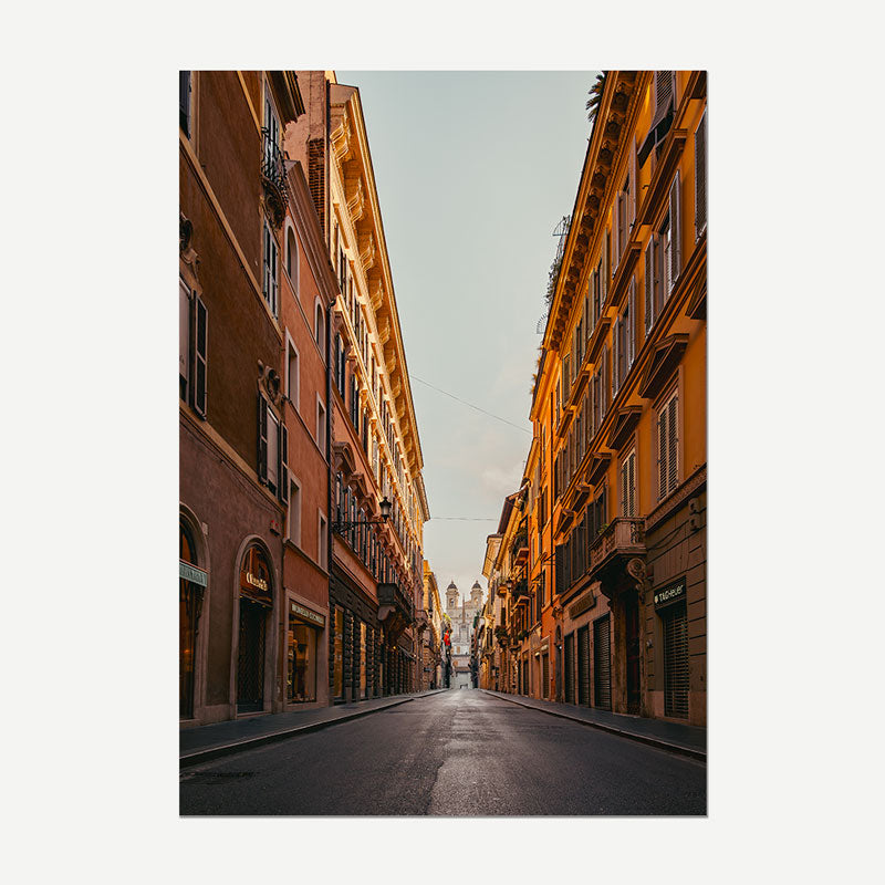 A vertical photographic print of a narrow European street lined with warm-toned buildings, shown centered on a light gray background.