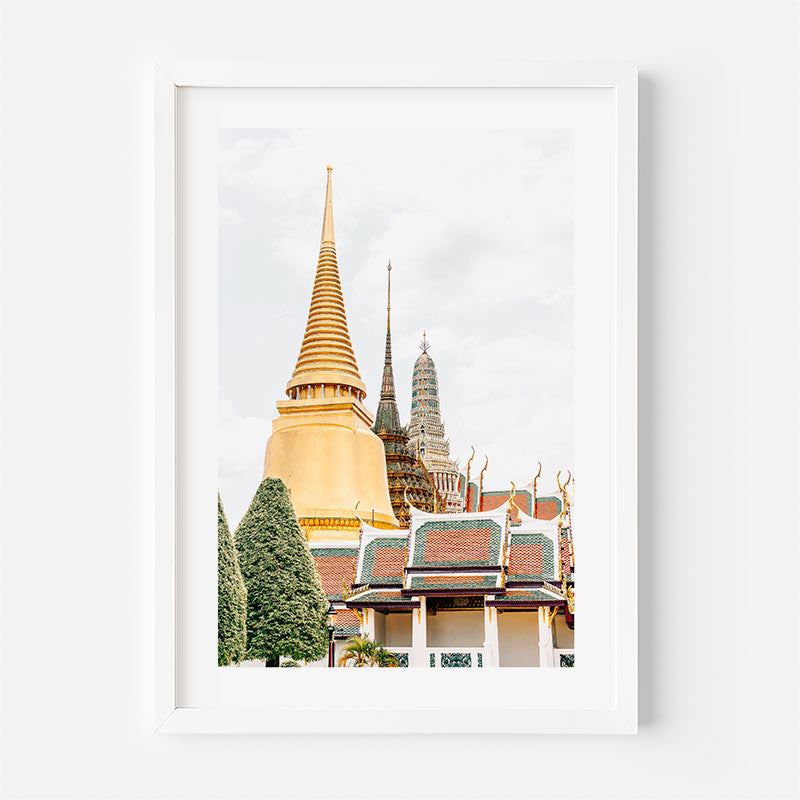 A framed art print featuring a photograph of a Thai temple with a large golden chedi and traditional tiled roofs, displayed on a clean white wall.