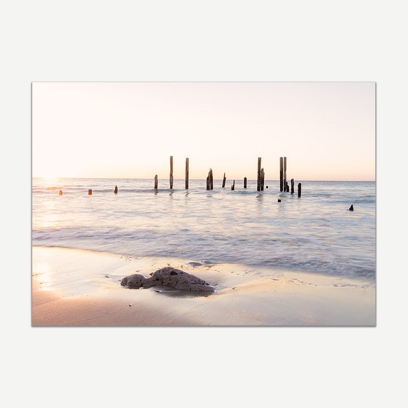 Beach scene with sunset, water, and wooden posts.