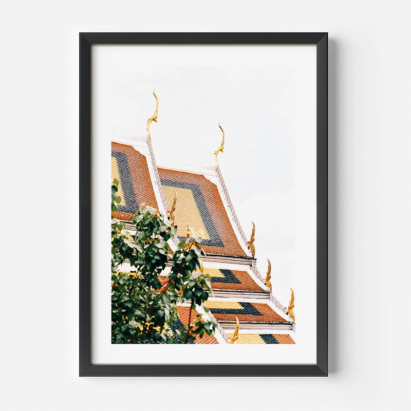 Framed wall art featuring a stylized architectural scene with a temple roof and green foliage, shown in a black frame against a white background.