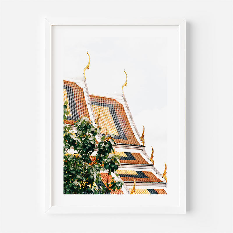 A framed art print featuring a low-angle photograph of the ornate golden roof spires of the Grand Palace in Bangkok, framed in a clean white frame against a white wall.