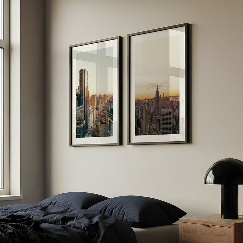 Two framed cityscape prints on a wall above a bed with dark bedding.
