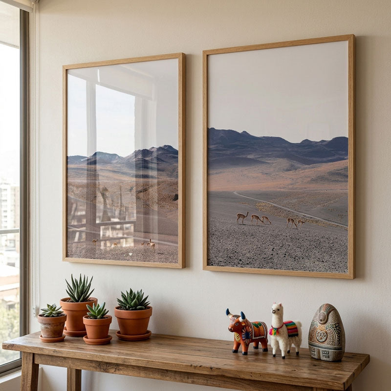 Two framed landscape pictures on a wall with a wooden table and decorative items below.