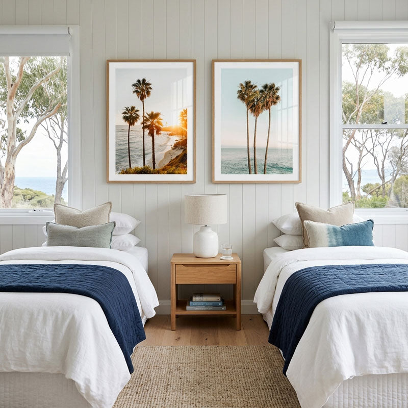 Two beds in a bedroom with beach-themed wall art and a lamp on a nightstand.