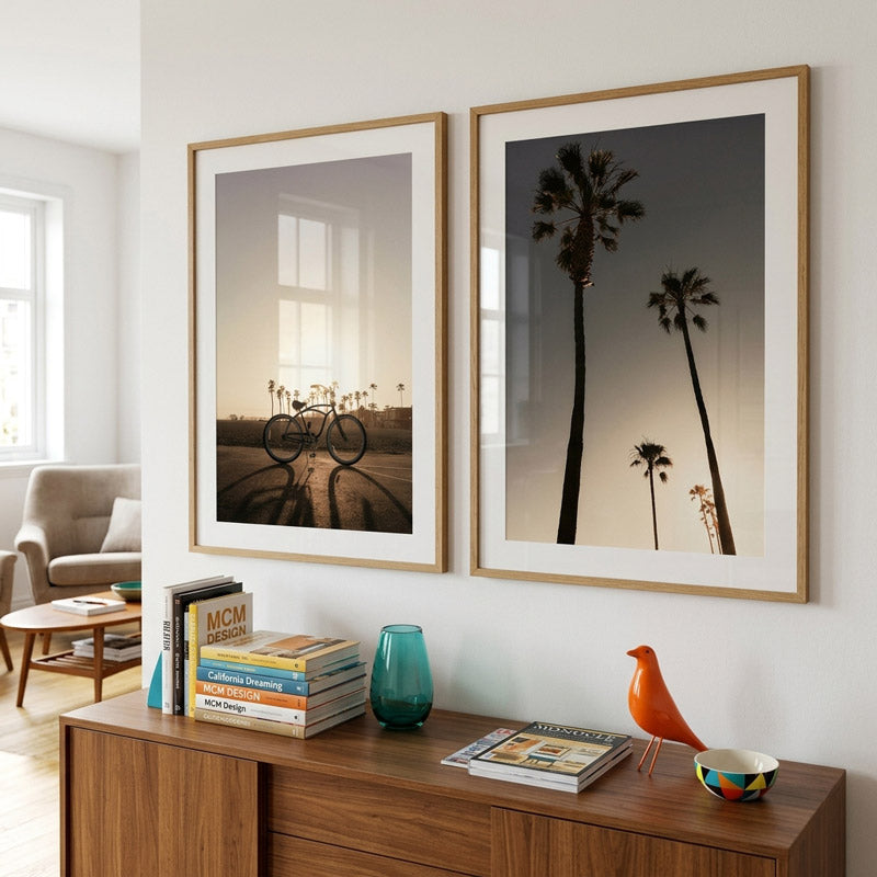 Two framed artworks of bicycles and palm trees on a wall above a wooden console table.