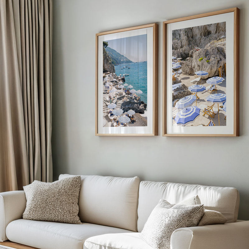Two framed beach scene prints above a white sofa with decorative pillows.