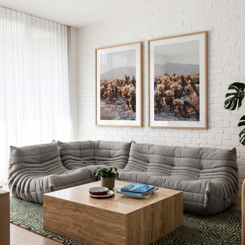 Modern living room with a gray sectional sofa, wooden coffee table, and two framed landscape pictures on the wall.