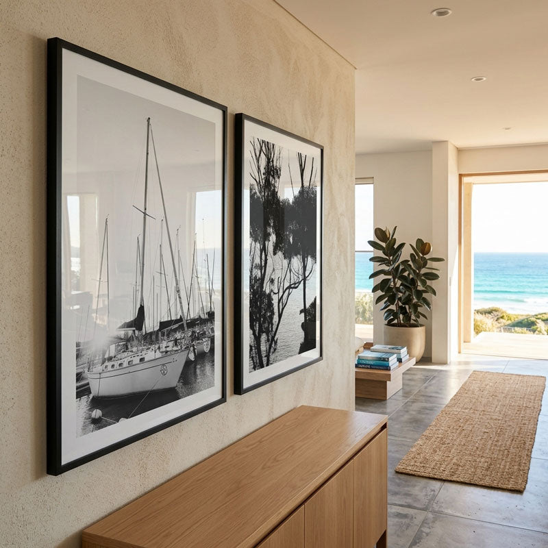 Two framed black and white artworks on a wall with a view of the ocean.