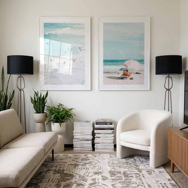 Modern living room with beach-themed artwork, white furniture, and decorative plants.