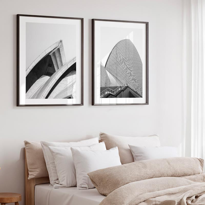 Two framed black and white artworks on a wall above a bed with neutral bedding.