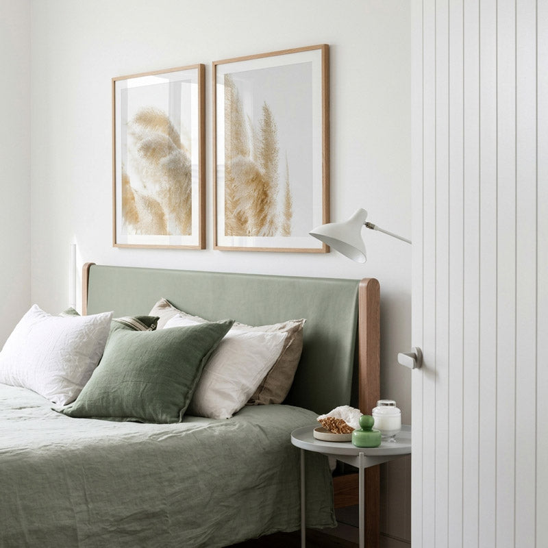 Neatly made bed with green bedding and pillows, nightstand with small items, and framed artwork on the wall.