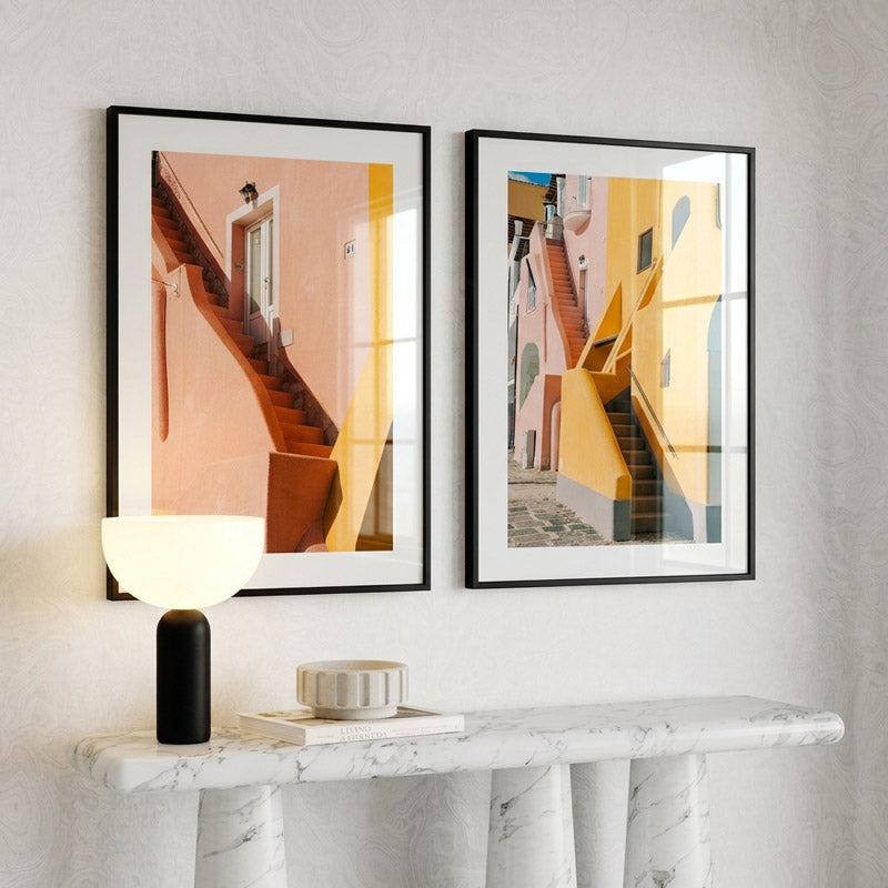 Two framed artworks of staircases on a wall above a marble console table.
