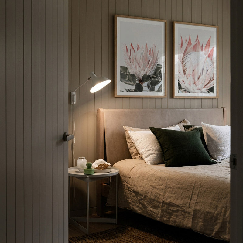 Cozy bedroom with floral wall art, bed with pillows, and side table.