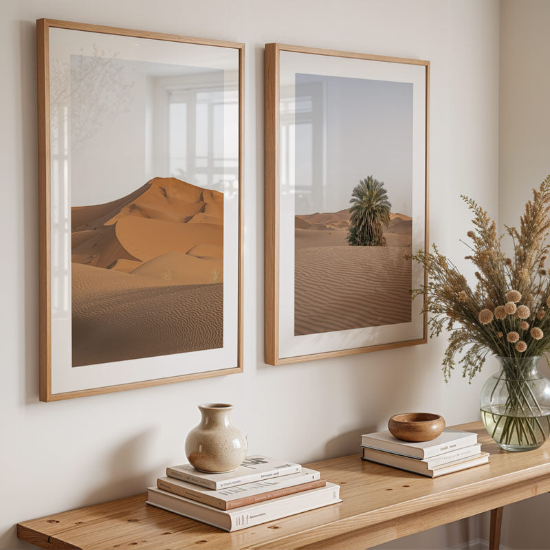Two framed desert landscapes on a wall above a wooden console table with decorative items.