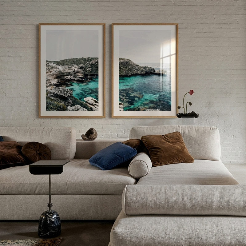 Modern living room with a beige sofa, decorative pillows, and framed ocean views on the wall.