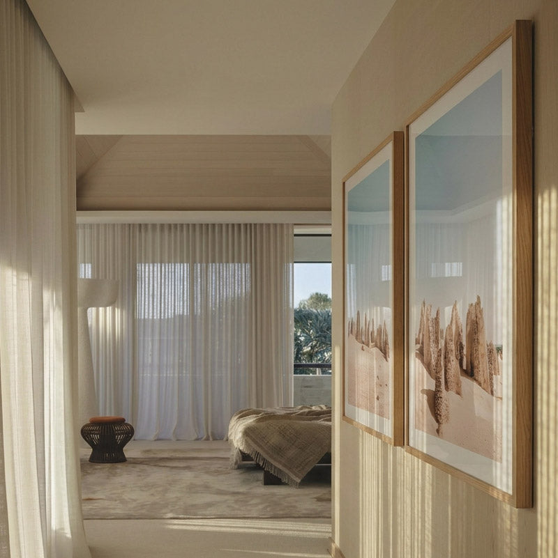 Modern bedroom with two framed artworks on a wall, leading to a bed and window.