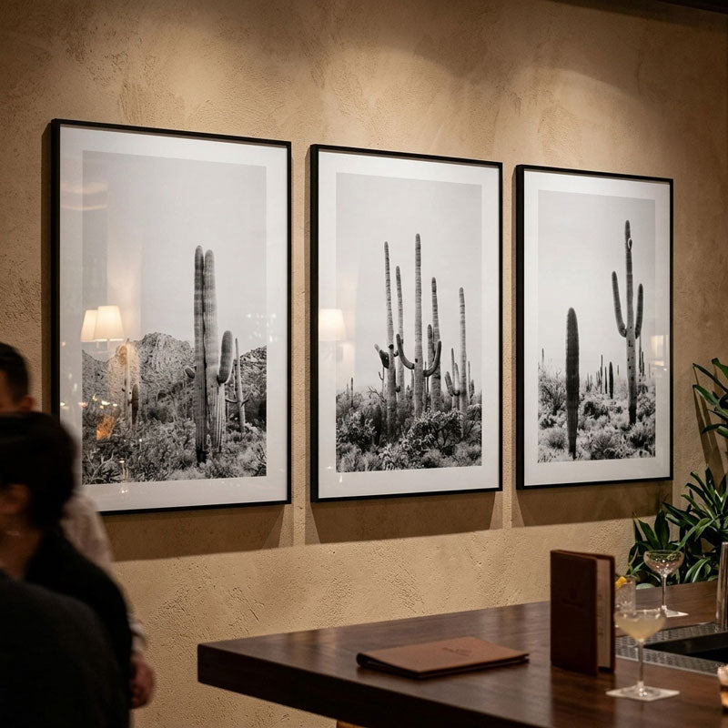 Three framed black and white photographs of cacti on a wall with a table and people in the foreground.