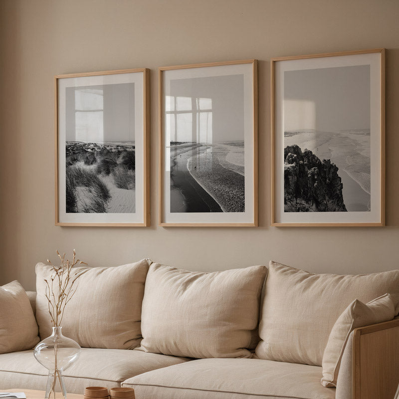 Three framed artworks above a beige sofa in a living room setting.