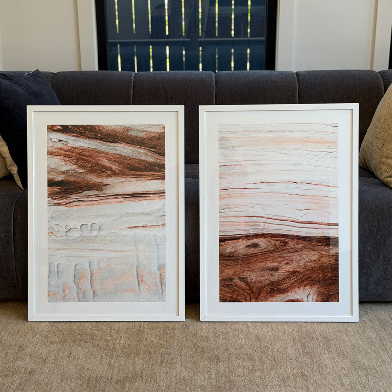 Two framed abstract artworks on a carpeted floor with a couch in the background.