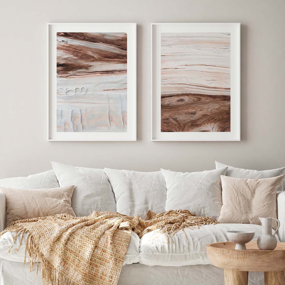 A pair of framed abstract prints featuring sand stone textures, displayed on a wall above a white sofa with neutral colored cushions.