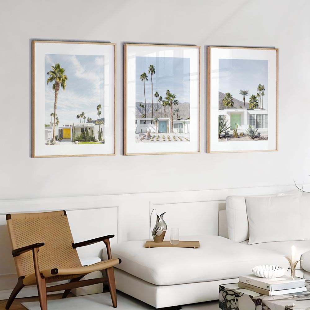 A set of three framed photographs featuring a yellow door, a blue door, and a mint green door, displayed on a wall over a white sofa with a wooden chair to the left.