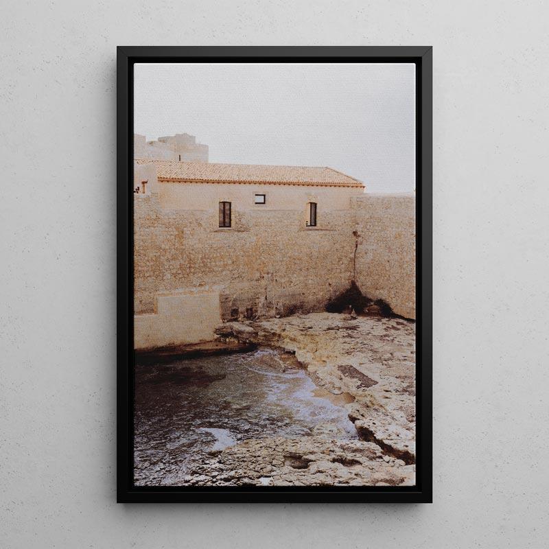 Framed photograph of a stone building and water feature on a white wall
