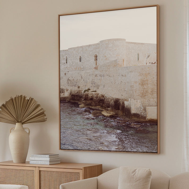 Framed artwork of a coastal scene with a castle on a wall in a living room.
