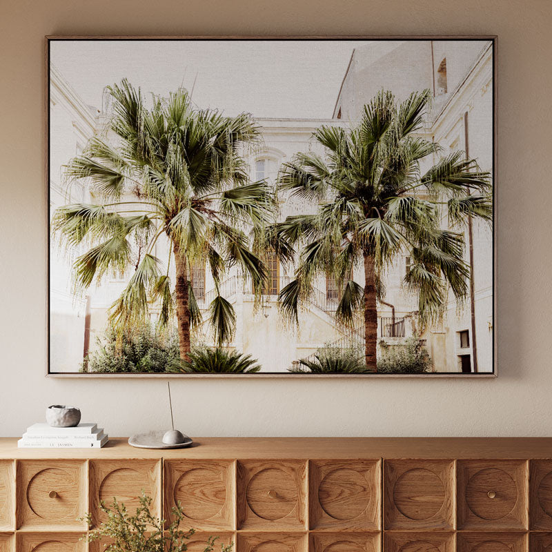 Framed artwork of palm trees on a wall above a wooden console table.