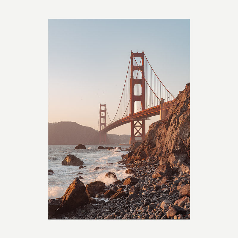 Golden Gate Bridge viewed from a rocky beach with water and mountains in the background