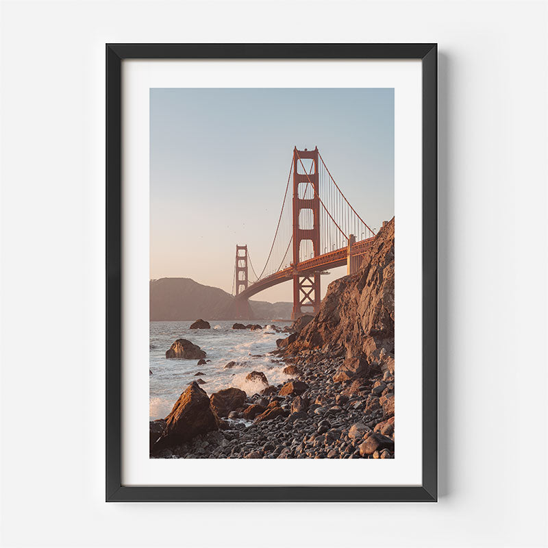 Framed photograph of the Golden Gate Bridge with a rocky shore and water.