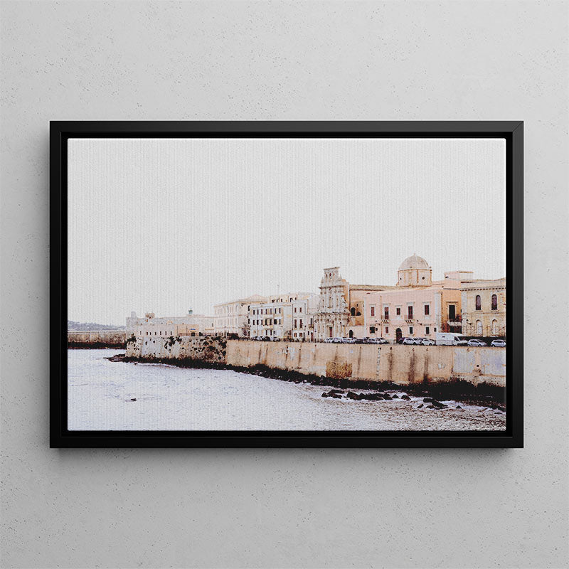Framed photograph of a coastal cityscape with buildings and water on a gray wall.