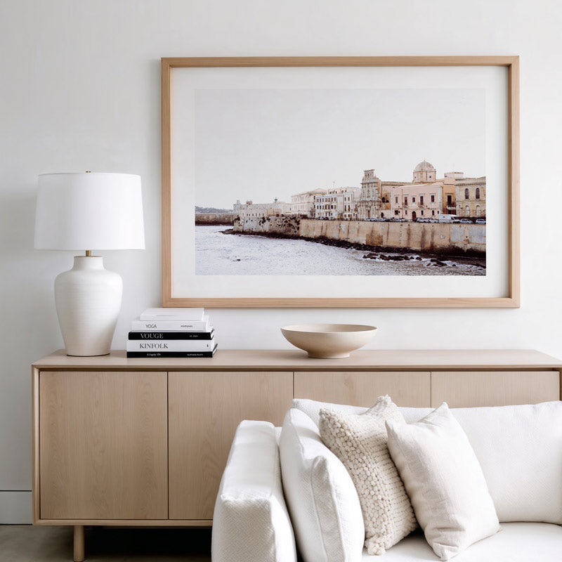 Living room with a wooden sideboard, white sofa, and framed picture of a coastal scene.