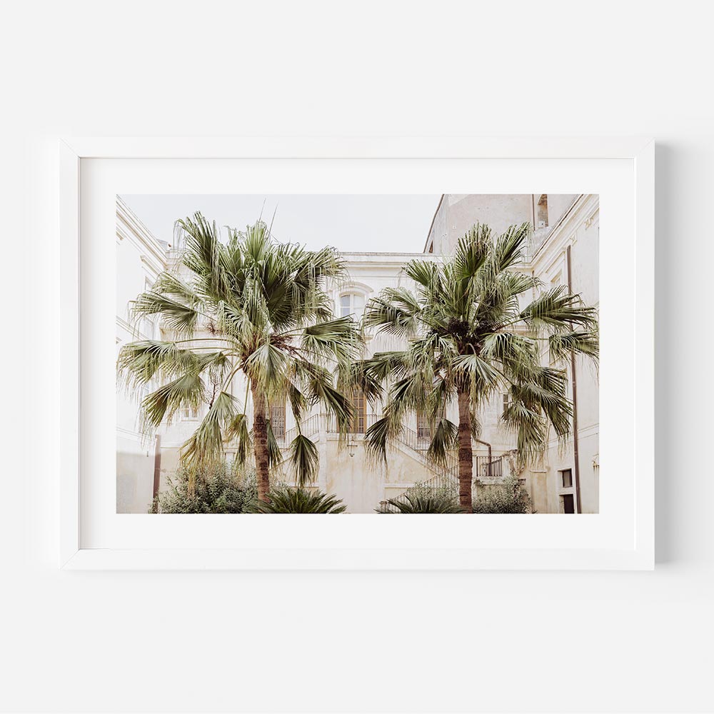 Framed coastal wall art showcasing twin palm trees nestled in a quiet Sicilian courtyard—captured in Syracuse, Italy. This beach scene wall art features soft neutrals, weathered textures, and timeless Mediterranean charm, ideal for beach art for wall and coastal décor.
