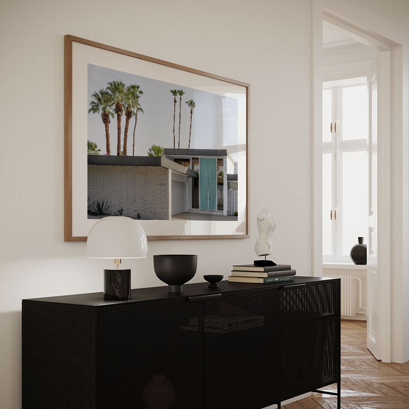 Modern interior with a black console table, lamp, and framed picture of palm trees.