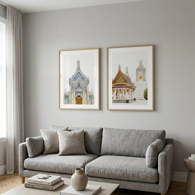 A modern living room scene with a light gray fabric sofa, two framed architectural art prints on a light gray wall, a window with sheer curtains, and a small wooden coffee table in the foreground.
