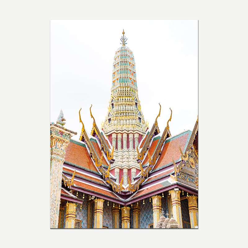 A vertical photographic print of the Grand Palace spire in Bangkok, showcasing its intricate gold, red, and green tiled architecture against a bright white sky, presented on a light gray background.