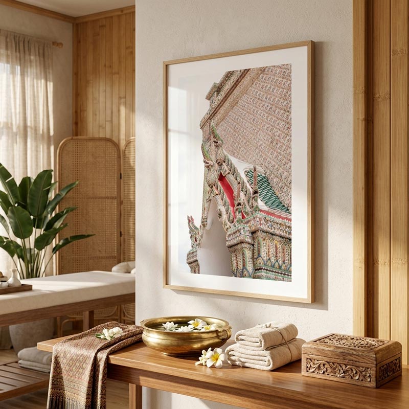 A framed art print featuring a close-up of a Thai temple with ornate multicolored carvings, displayed on a beige wall in a warm, modern bohemian-style room with wooden furniture and decor.