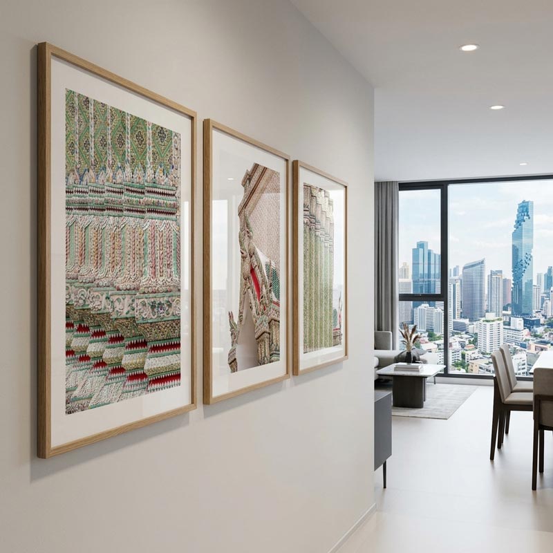 Three framed vertical art prints with intricate architectural and decorative patterns hang on a light gray wall in a modern living room with a city view.